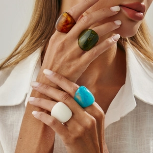 Detailed view of chunky resin rings in amber, green, blue, and matte white on a model