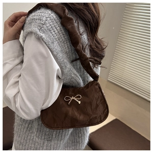 Brown underarm bag with gold bow detail and pleated texture strap on a female model