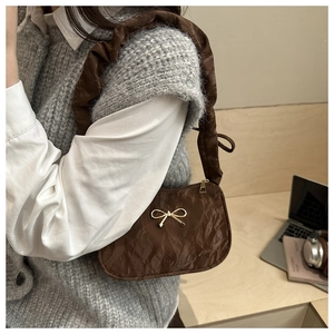 Détail d'un sac bandoulière matelassé marron avec nœud doré et bandoulière à volants