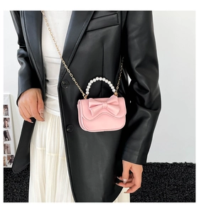 Detail of pink bow handbag with pearl handle and golden chain strap on a model
