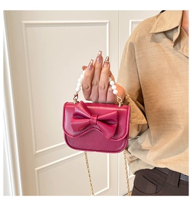 Dettaglio borsa fucsia con grande fiocco, manico di perle e tracolla a catena dorata