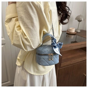 Dettaglio borsa cilindrica trapuntata azzurra con catena e foulard a pois sul manico