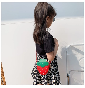 Detail of red strawberry-shaped children's crossbody bag with green leaf and silver studs