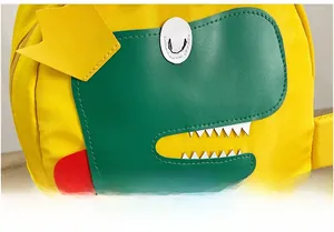 Dettaglio dello zaino giallo per bambini con toppa a forma di dinosauro verde e corona