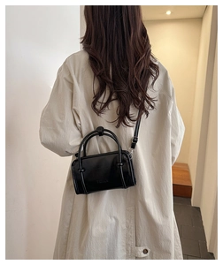 Detail of a black square leather bag with Fashion text worn over a beige trench coat