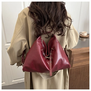 Detail of wine red leather shoulder bag with gold hardware worn on a khaki trench coat