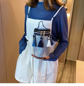 Dettaglio della borsa a cilindro intrecciata con nappe etniche e motivi geometrici blu