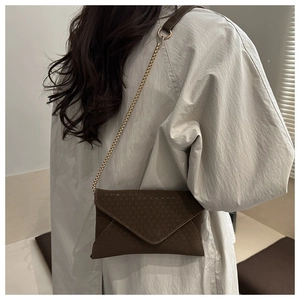 Detail of dark brown suede envelope bag with gold chain strap on a trench coat