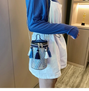 Dettaglio di una borsa a secchiello intrecciata cilindrica con nappe blu e catenina