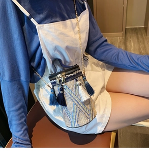 Dettaglio di una borsa a secchiello in paglia con nappe blu e tracolla a catena dorata