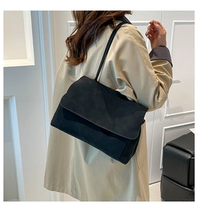 Detailed view of black suede tote bag with flap closure worn with a beige trench coat