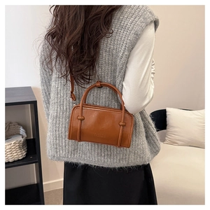 Detail of caramel leather crossbody bag featuring embossed FASHION logo and slim handles