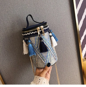 Dettaglio borsa a secchiello boho in paglia con nappe blu e tracolla a catena d'oro
