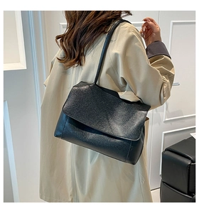 Detail of black textured leather shoulder bag with flap closure and slim strap