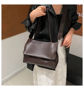 Detail of dark brown leather tote bag with wide adjustable strap worn by a model