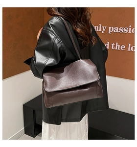 Detail of dark brown leather tote bag with minimalist flap design on a shoulder model