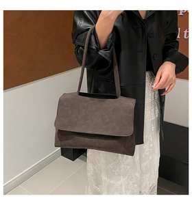 Detailed close-up of dark brown suede shoulder bag with long strap and minimalist flap design