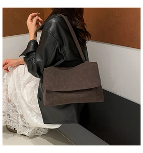 Detail of soft dark brown leather flap bag showing matte texture and wide shoulder strap