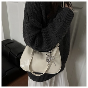Detail of a chic cream-colored shoulder bag with silver bow and heart charms on a model