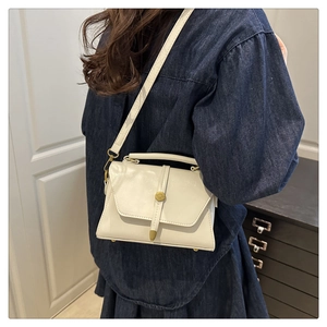 Détail du sac en cuir crème avec fermoir anneau doré et poignée porté par un mannequin