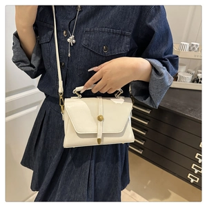 Detailed view of cream white crossbody bag with gold buckle on a minimalist cabinet