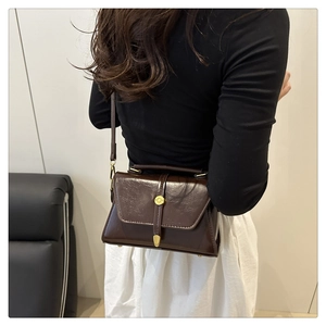 Detail view of dark brown leather crossbody bag with vintage gold metal buckle on model