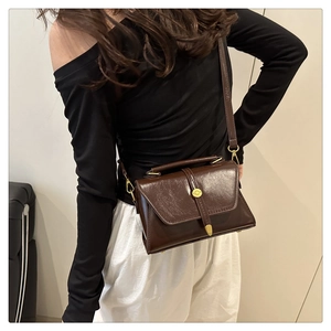 Detail van een donkerbruine leren crossbodytas met bronzen gesp en riem in vintage stijl