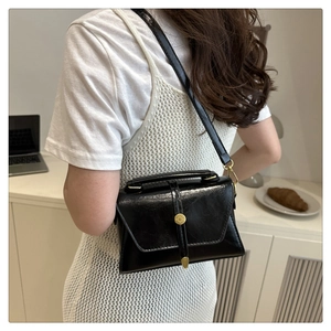 Achteraanzicht van glanzende zwarte crossbodytas met gouden gesp op een model