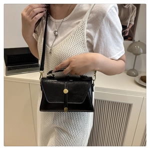 Detail of a black leather crossbody bag with elegant gold vertical buckle on white desk