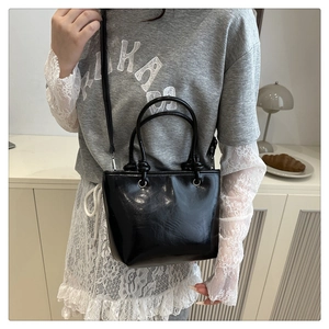 Detail view of shiny black patent leather crossbody bag with silver hardware and top handle