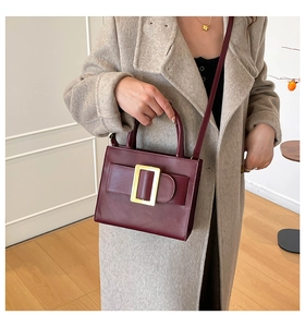 Detail of burgundy leather handbag featuring a signature large gold metal buckle closure