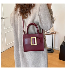 Detail of burgundy leather handbag with gold buckle accessory on a grey wool coat