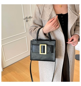 Detail of vintage black crossbody bag with large gold square buckle on a beige coat