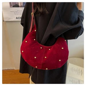 Dettaglio della borsa hobo in velluto bordeaux con borchie dorate portata a spalla