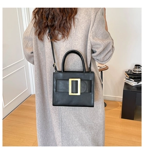 Detail of a minimalist black square handbag with golden buckle worn with a beige coat