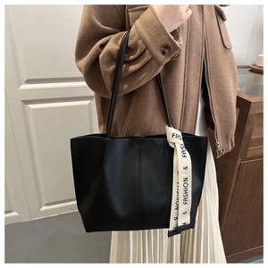 Dettaglio di una borsa tote in pelle nera con cuciture verticali e nastro decorativo