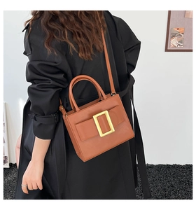 Detail of a brown leather structured handbag with a gold square buckle on a black coat