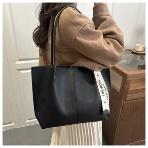 Dettaglio di una borsa tote nera in similpelle con nastro su un cappotto color cammello