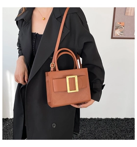 Close-up of brown leather handbag featuring a large gold buckle and sturdy top handles