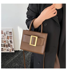 Detail of a brown leather handbag featuring a large golden square buckle and dual handles