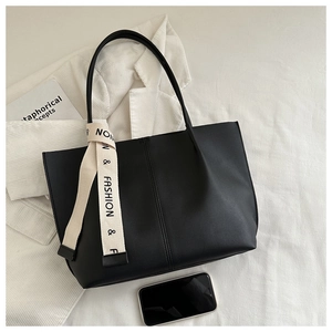 Dettaglio macro della borsa tote nera opaca con tracolla stampata su blazer bianco