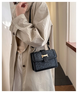 Close-up of black retro crossbody bag featuring golden buckle and monogram print