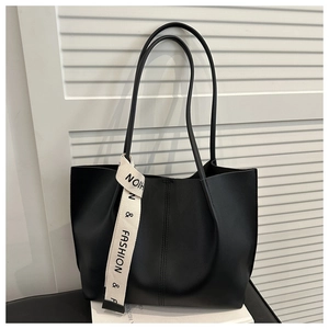 Dettaglio di una borsa tote nera opaca con cuciture verticali e ciondolo a nastro fashion