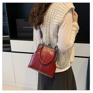 Detail view of burgundy leather kiss-lock bag with white stitching and metal frame
