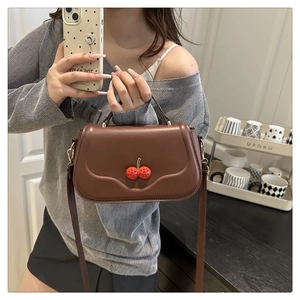 Detail of a brown PU leather handbag featuring a red cherry rhinestone metal clasp