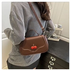 Detail of dark brown leather underarm bag with red cherry crystal buckle on knitwear