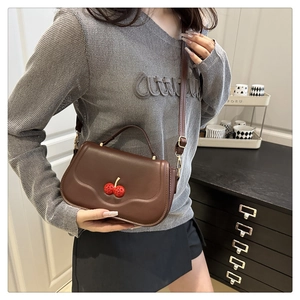 Detail of a brown leather cherry flap bag with a crossbody strap on a sweater model