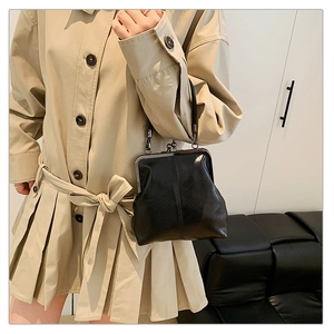 Detail of a black shiny leather shell bag with metal clasp, styled on a khaki trench coat