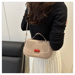 Detail of a beige leather cherry purse worn by a model in a minimalist modern setting