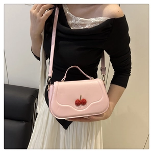 Close-up of pink crossbody bag with cherry clasp and handle shown on a model